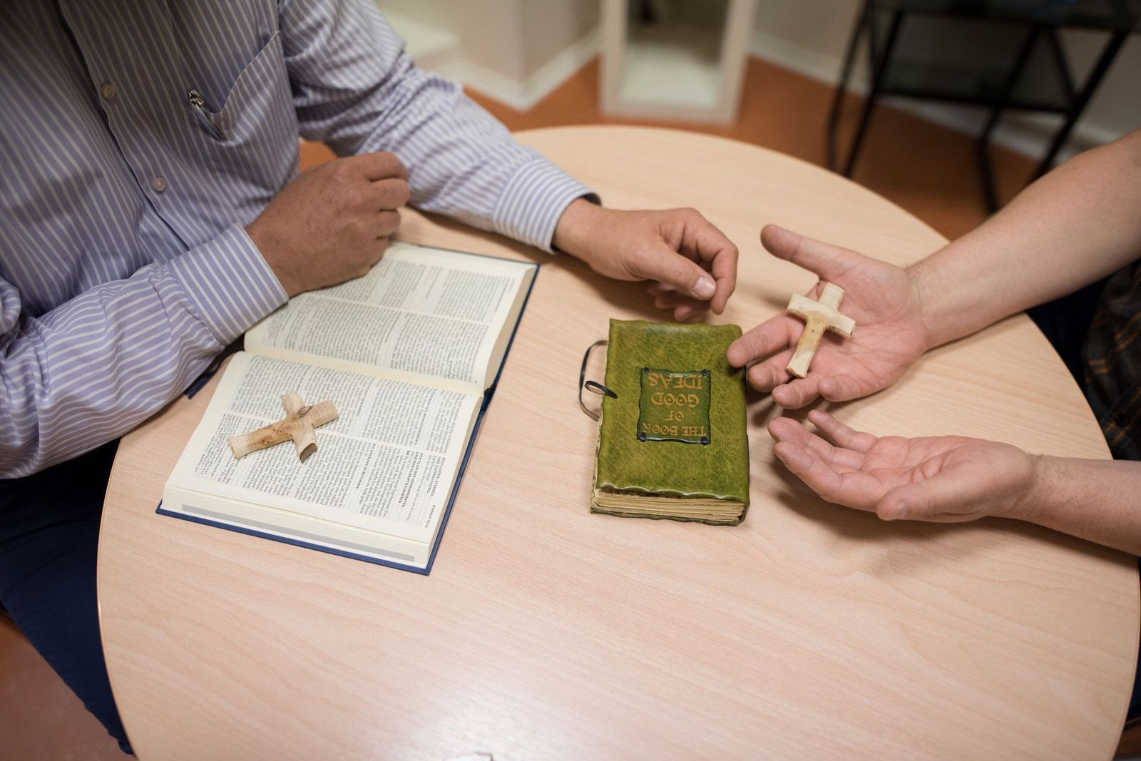 Der Bildausschnitt zeigt zwei Personen an einem Tisch mit aufgeschlagener Bibel und kleinen Holzkreuzen