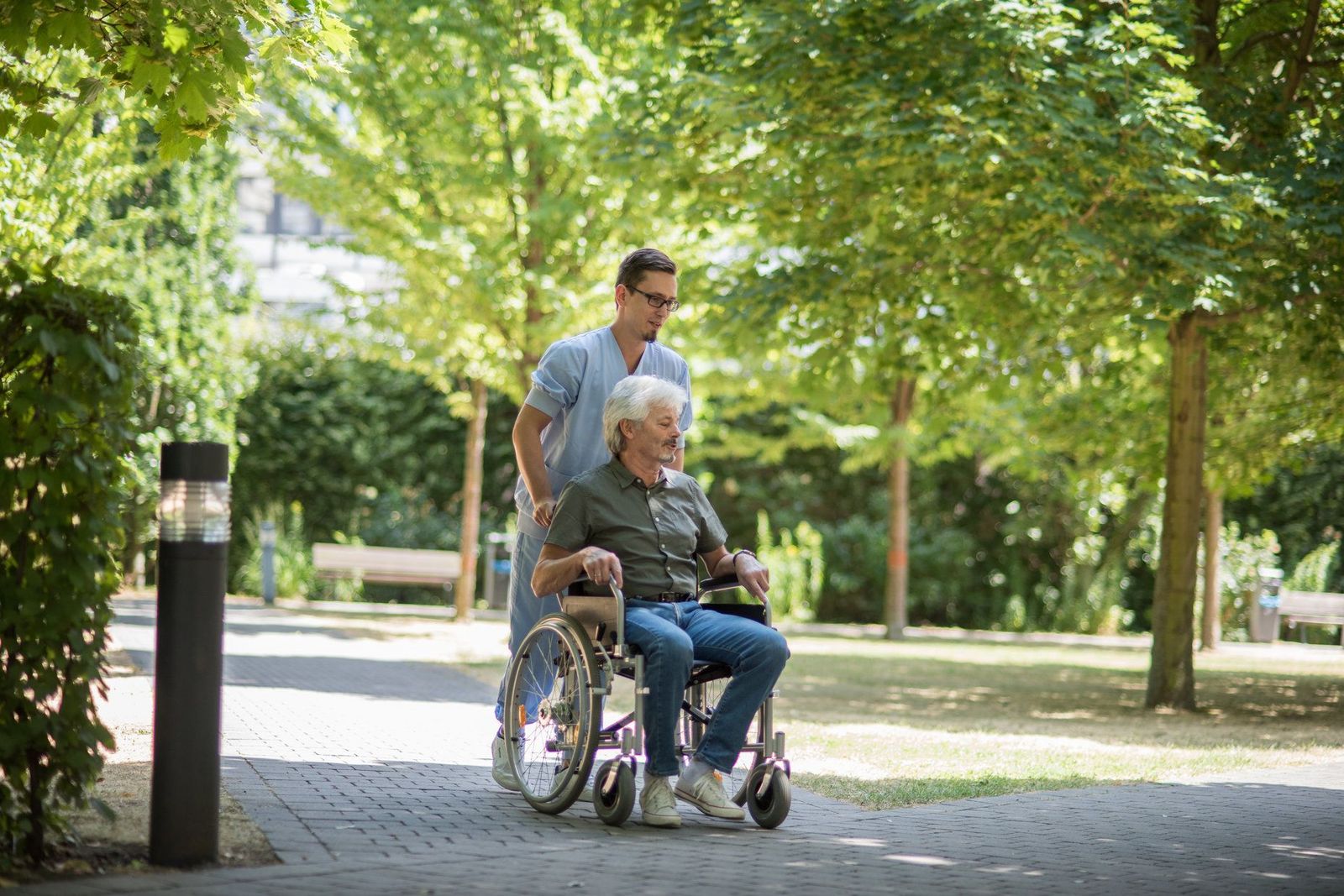 Gesundheits- und Krankenpfleger mit einem Herrn im Rollstuhl im Krankenhausgarten